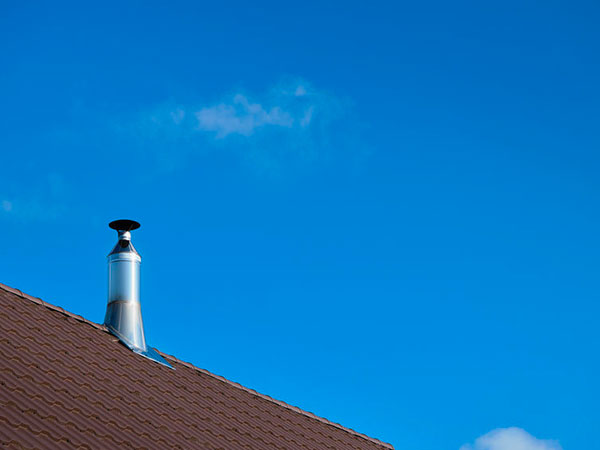 Modern style chimney from oven or fireplace stacked stainless steel on tiled roof made according to fire safety requirements and to avoid condensation when reaching dew point in flue gases. pulizia-canne-fumarie